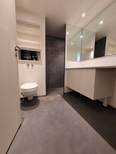 Microcement badeværelse med mørkt gulv og væghængt toilet
